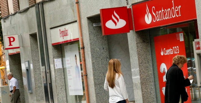 Un par de personas utilizan un cajero automático de una oficina del Banco Santander, en Barcelona, situada junto a una sucursal del Popular. REUTERS/Albert Gea