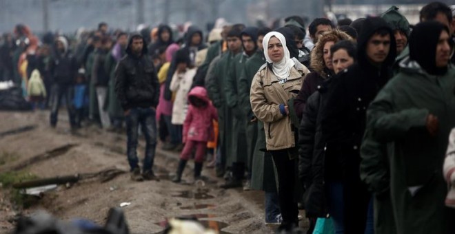 Refugiados y migrantes guardan cola bajo la lluvia para recibir una taza de café o té mientras esperan en un campo de refugiados cerca de Idomeni (Grecia). - EFE