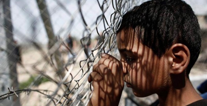 Un niño se apoya en una valla durante una manifestación por la apertura de las fronteras a Macedonia en el campo improvisado de refugiados de Idomeni. / KOSTAS TSIRONIS (EFE)