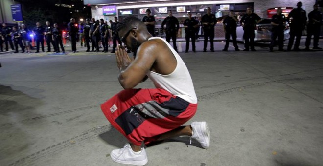 Un joven se arrodilla frente a los policías desplegados en la esquina de Ross Avenue y Griffin street durante la manifestación contra la violencia policial hacia los negros en EEUU./ EFE