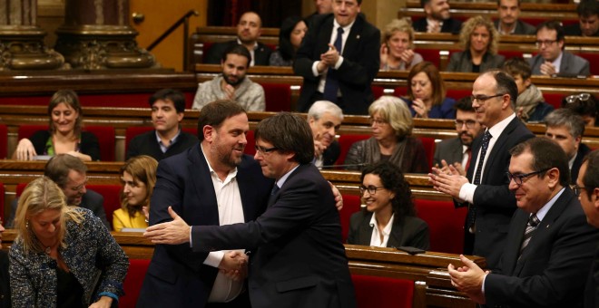 El presidente de la Generalitat, Carles Puigdemont, felicita al vicepresidente y conseller de Economía, Oriol Junqueras, al finalizar la votación en la que el Govern ha conseguido la admisión a trámite de la Ley de Presupuestos con el apoyo crítico de la