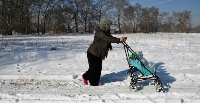 Una mujer empuja por la nieve el carro con su hijo en un campo de refugiados en Grecia. REUTERS