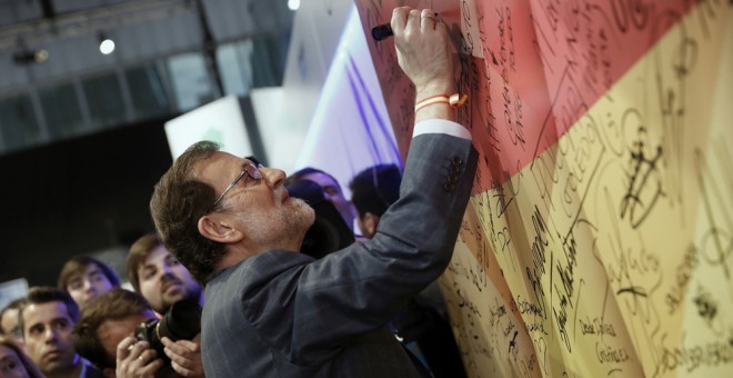 El presidente del Gobierno y líder del PP, Mariano Rajoy, firma en una bandera española a su llegada a la segunda jornada del XVIII Congreso nacional del partido en la Caja Mágica, en Madrid. EFE/Javier Lizón