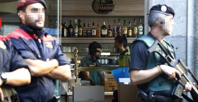 Efectivos de la Guardia Civil y los Mossos d'Escuadra durante el registro realizado en una cafetería en los bajos del edificio en que se encuentra el Consulado italiano de la calle Mallorca, en Barcelona. | MARTA PÉREZ (EFE)