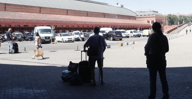 Pasajeros esperan en la estación de Atcocha en madrid, sus compañeros taxistas en huelga se concentran frente a la parada de la estación de Atocha en Madrid.-EFE/Zipi