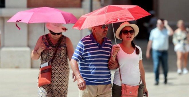 Varias personas recorren el casco antiguo de la ciudad protegidos con parasoles cuando la Consejería de Sanidad, según las predicciones del Centro de Estudios Ambientales del Mediterráneo (CEAM), ha activado para hoy la alerta sanitaria por nivel alto o n