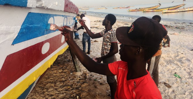 Varios hombres pintan un bote de pesca en una playa en Dakar. REUTERS / Edward McAllister