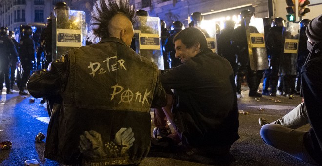 Dos jóvenes manifestantes hablan distendidamente mientras están sentados en primera línea de la barrera frente a los antidisturbios de los Mossos en Urquinaona. GUILLEM SANS.