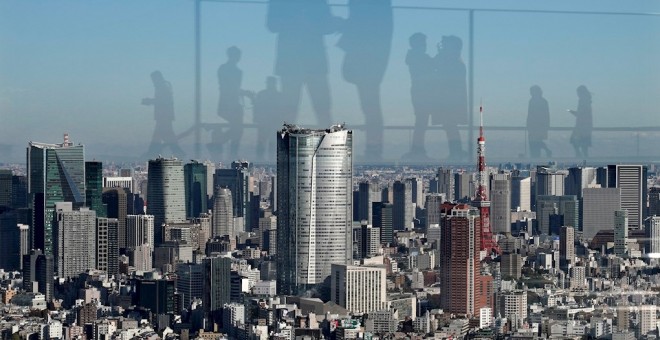 Los visitantes se reflejan en el vidrio acrílico de una plataforma del mirador en un edificio desde donde se observa el centro de  Tokio (Japón). EFE / EPA / KIMIMASA MAYAMA