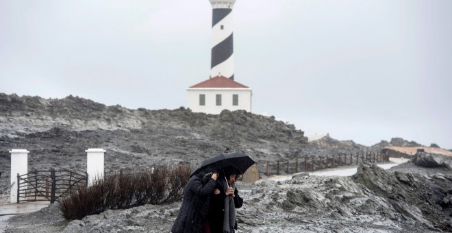 Dos personas caminan por las inmediaciones del faro de Faváritx, en el municipio de Mahón, en una jornada en la que la borrasca Gloria, que trae este domingo un temporal de lluvia, nieve, viento y olas, ha puesto en alerta roja a la Comunidad Valenciana