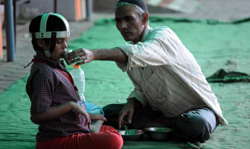 Un hombre da de comer a un niño, víctima de segunda generación de la catástrofe de Bhopal. // AFP