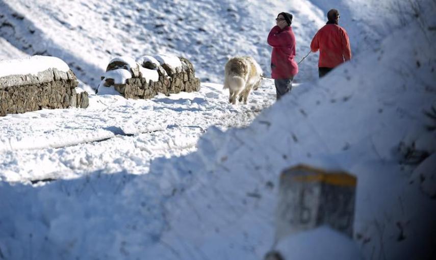 Dos personas pasean por la carretera comarcal CA-643 en la subida al puerto de Lunada por la red secundaria donde es obligatorio el uso de cadenas y donde esta activada la alerta por nevadas. EFE/Pedro Puente Hoyos