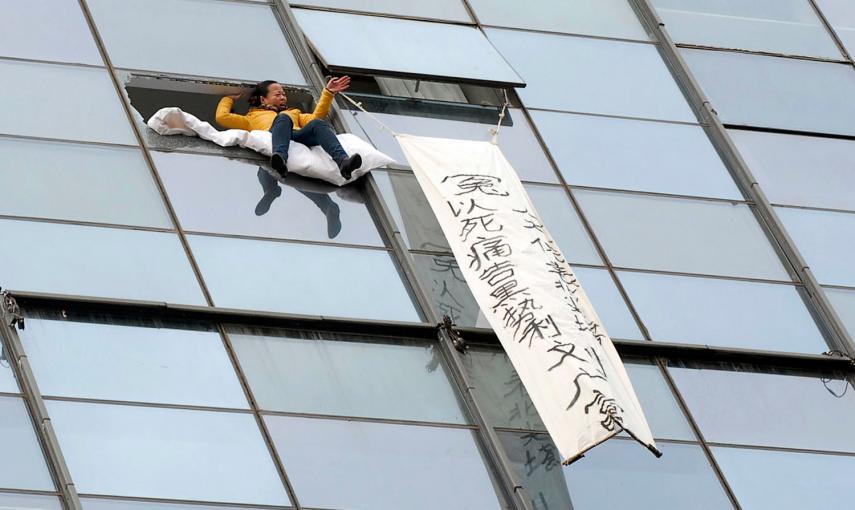 Una mujer se sienta en el borde de una ventana que previamente ha roto, al lado de una bandera anunciando su intención de suicidarse por una disputa financiera con en funcionario del gobierno local, según los medios. La mujer finalmente se arrojó al vacío