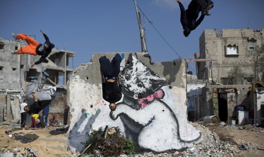 Jovenes palestinos hacen parkour junto a una pintada del artista británico Banksy. / AFP