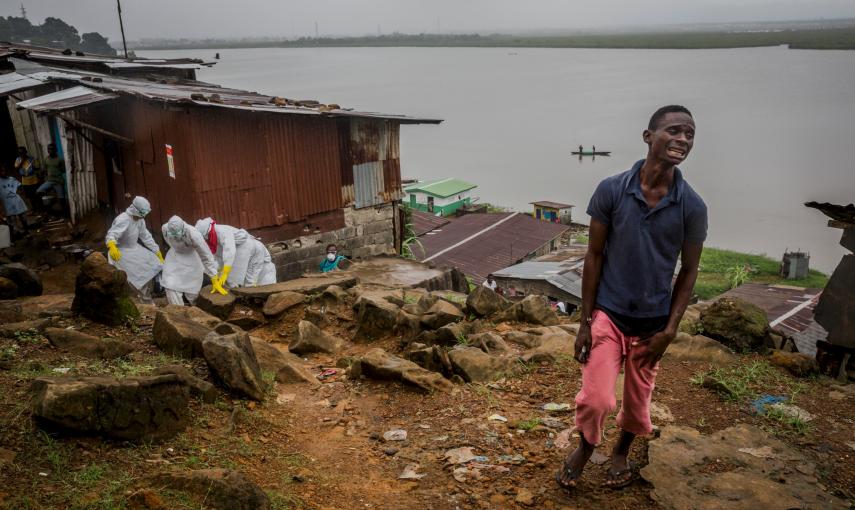 Eric Gweah, 25, observa como los miembros del equipo de entierros de la Cruz Roja llevan el cuerpo de su padre, Ofori Gweah, 62, una victima del Ébola, en la zona del rio Rock Spring Valley en Monrovia central, Liberia./ REUTERS/Daniel Berehulak/The New Y