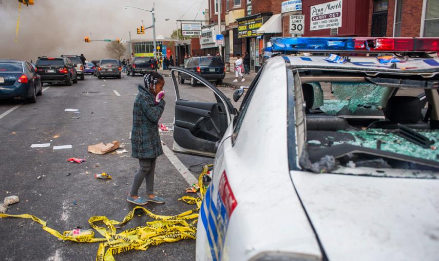 Una niña observa un vehículo de la policía que fue atacado durante protestas tras del funeral de Freddie Gray el lunes en Baltimore. EFE