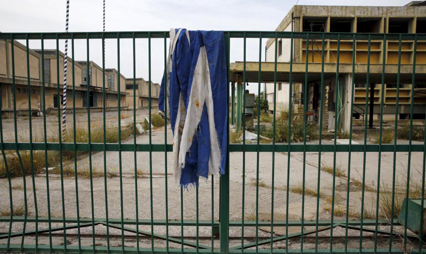 Una bandera griega sobre la puerta de una fábrica de aceite de cocina desierta que se cerró en 1996 en la ciudad de Elefsina, en la región Sterea Hellas, Grecia.- REUTERS / Yannis Behrakis