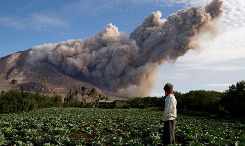 Un residente en su huerta mientras al fondo el volcán Monte Sinabung arroja cenizas.- BEAWIHARTA (REUTERS)