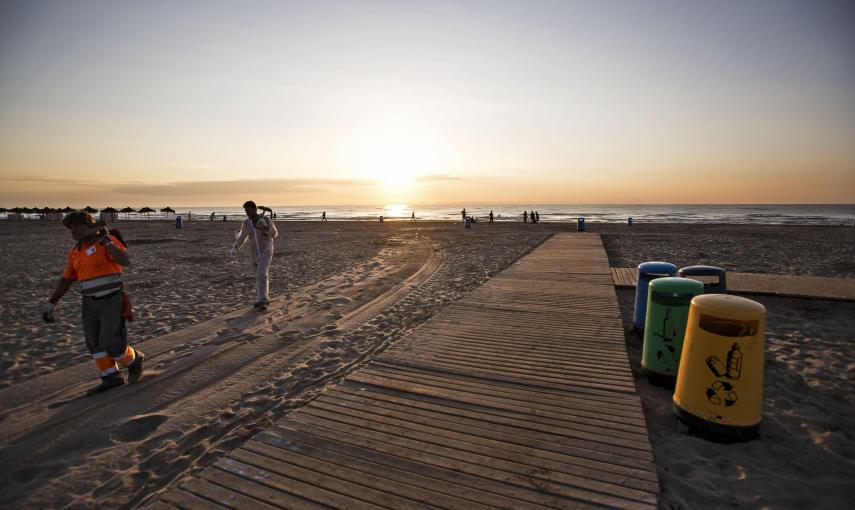 Dos trabajadores de los servicios de limpieza del ayuntamiento de Valencia se retiran de la playa de Las Arenas tras retirar los restos de basura tras la festividad de las Hogueras San Juan. /EFE/Manuel Bruque