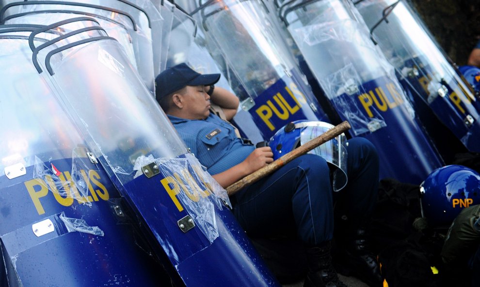 Un policía se apoya en escudos antidisturbios antes de su despliegue para bloquear los manifestantes que marchan hacia el parlamento en los suburbios de Manila, horas antes de que el presidente Benigno Aquino pronuncie su discurso anual. AFP PHOTO / Jay D