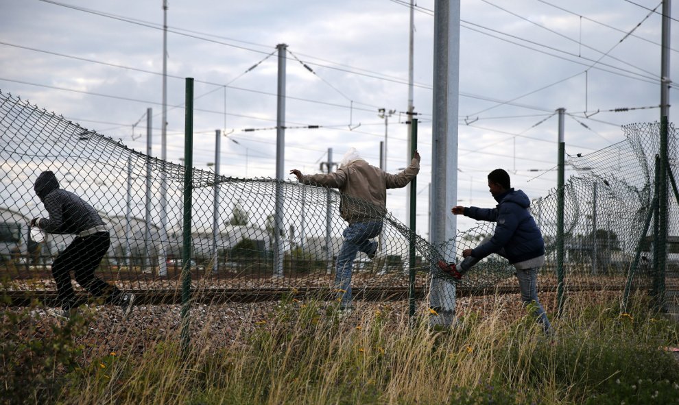 Inmigrantes cruzan una valla al tratar de llegar al tren que los conduciría a Inglaterra. EFE/YOAN VALAT