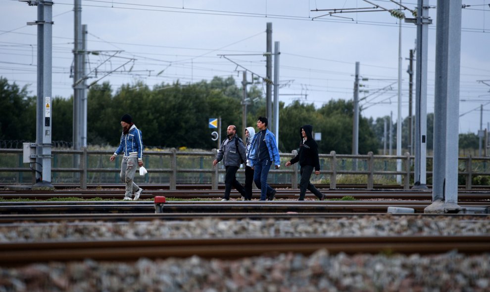 Inmigrantes caminan sobre una vía férrea para tratar de llegar al tren que los conduce a Inglaterra. EFE/YOAN VALAT