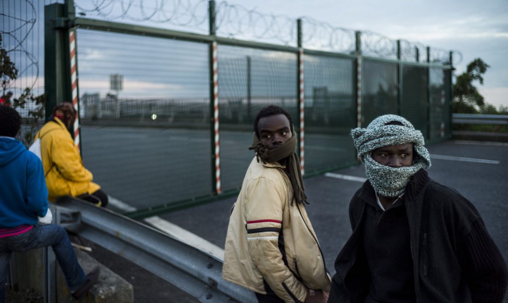 Migrantes esperan saltar una cerca para tomar un tren en su ruta hacia Inglaterra.- EFE