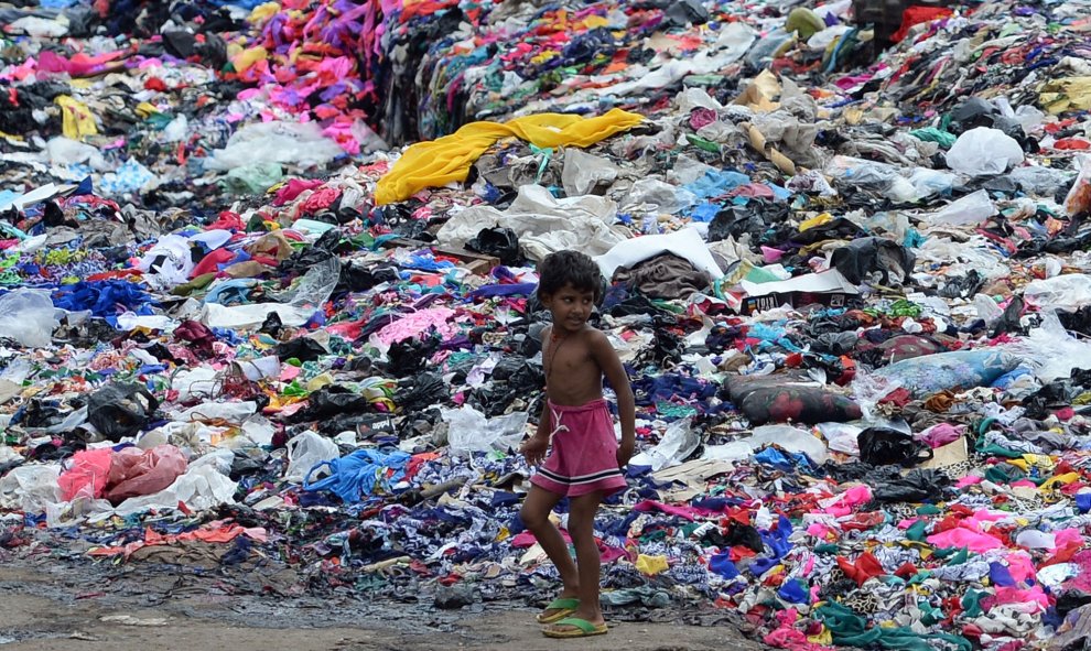 Un niño indio pasa junto  a un montón de piezas de tela en Mumbai el 15 de septiembre de 2015. AFP PHOTO / INDRANIL MUKHERJEE