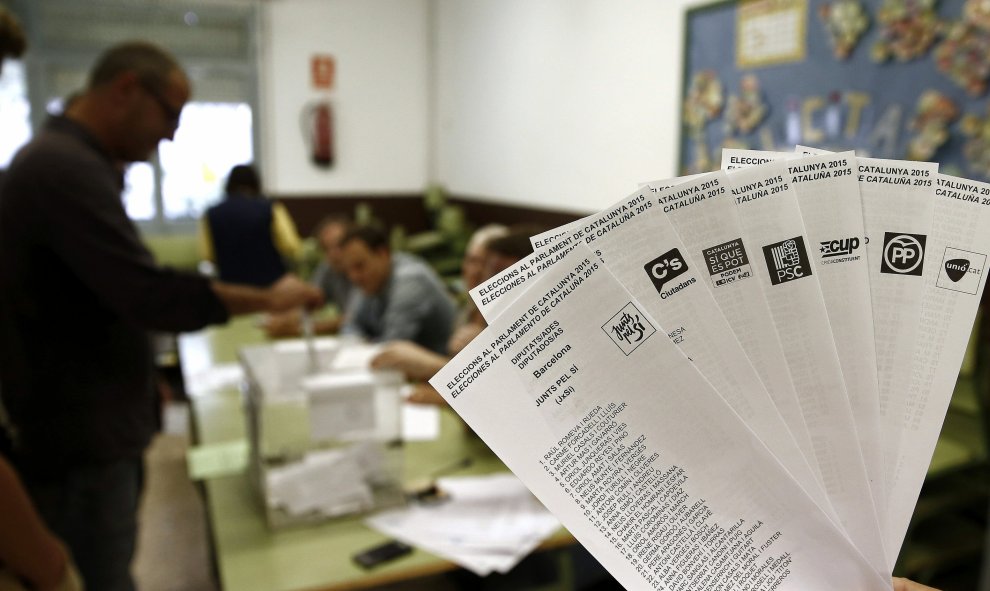 Una persona muestra las papeletas de los diferentes partidos que concurren a las elecciones al Parlament, mientras una persona deposita su voto en la urna. EFE/ Jesús Diges