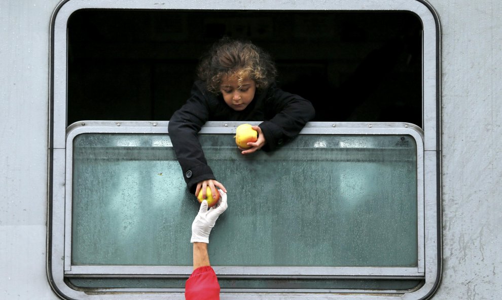 Una niña emigrante se asoma por la ventanilla del tren para coger comida en la estación de Tovarnik, en Croacia. REUTERS/Antonio Bronic