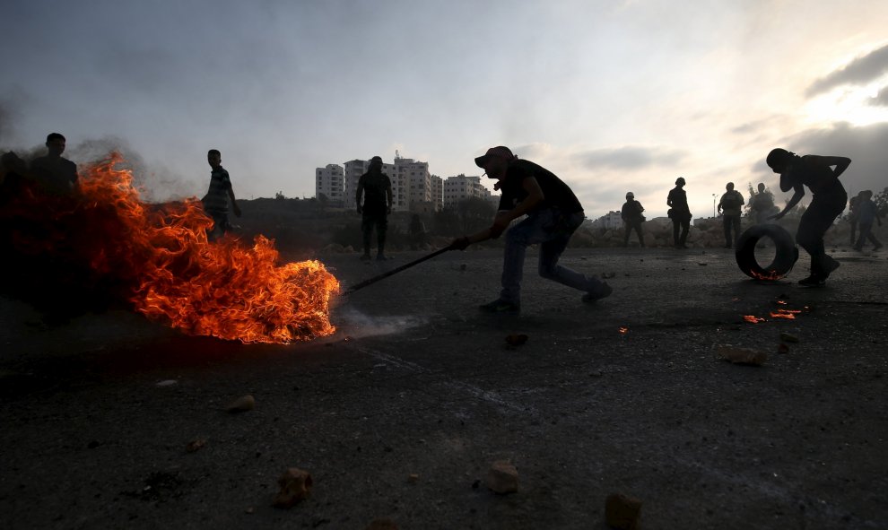 Palestinos mueven un neumático ardiendo durante enfrentamientos con el ejército israelí cerca del asentamiento judío de Bet El, cerca de la ciudad ocupada de cisjordana de Ramala, 5 de octubre de 2015. REUTERS/Mohamad Torokman