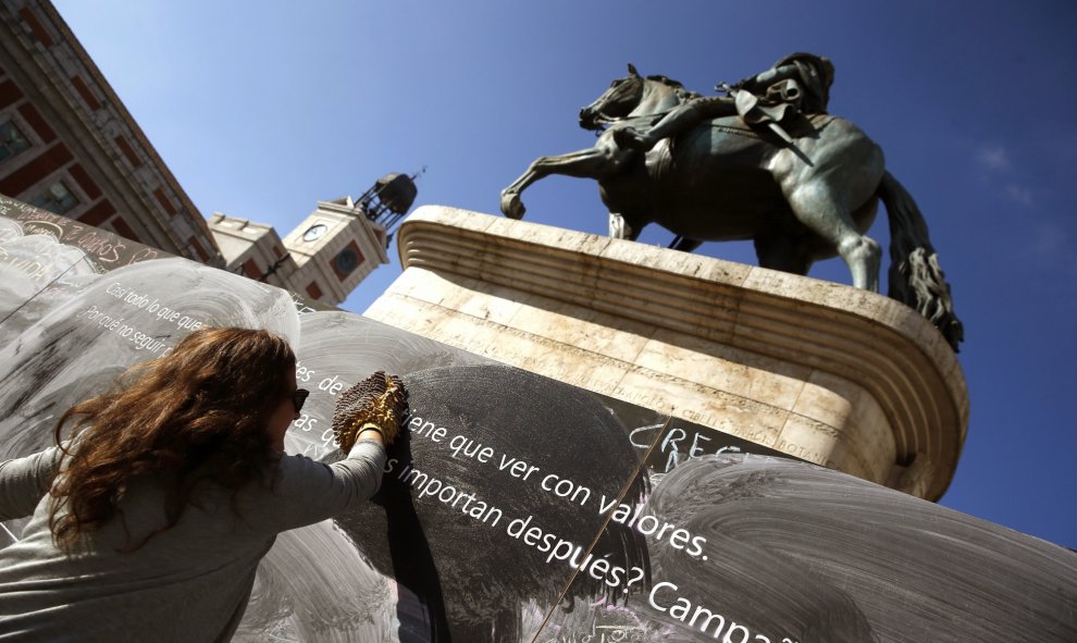 Una mujer limpia una pizarra mural instalada en la Puerta del Sol de Madrid, que parte de una iniciativa de la ONG "Alianza por la Solidaridad". EFE/Javier Lizón