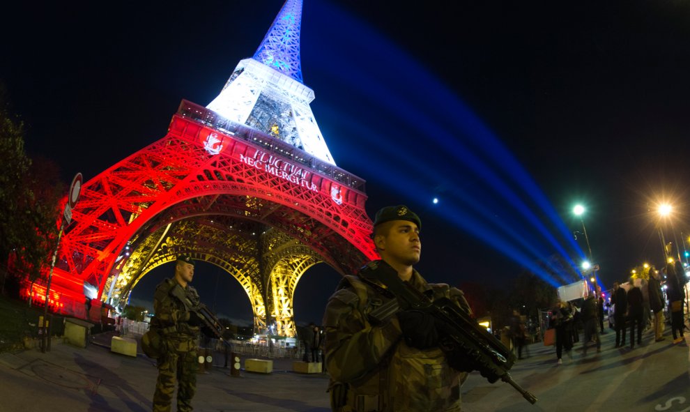 Un soldado francés monta guardia tras declararse una alerta de seguridad en Francia, frente a la Torre Eiffel,iluminada con los colores de la bandera francesa en homenaje a las víctimas de los atentados de París.-  AFP PHOTO / JOEL SAGET