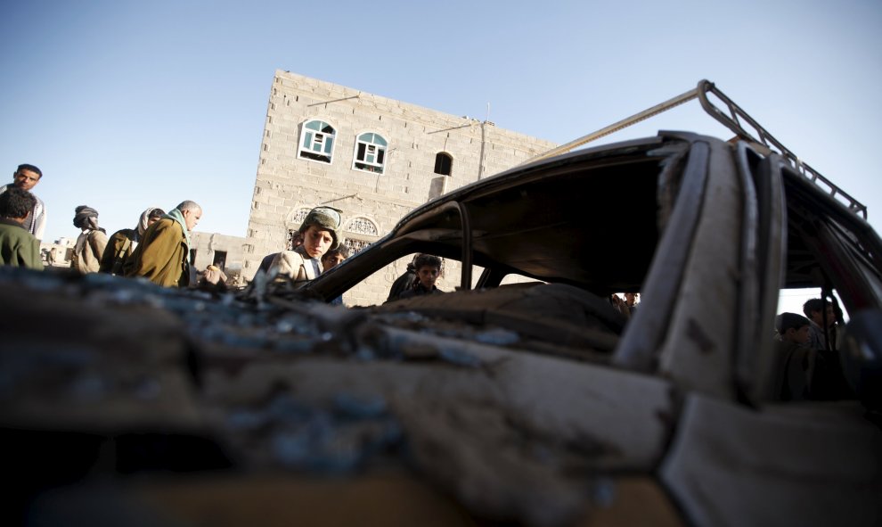 La gente se reúne alrededor de un coche dañado por un ataque aéreo saudita llevado a cabo a las afueras de la capital de Yemen, Saná, 29 de diciembre de 2015. REUTERS / Khaled Abdullah