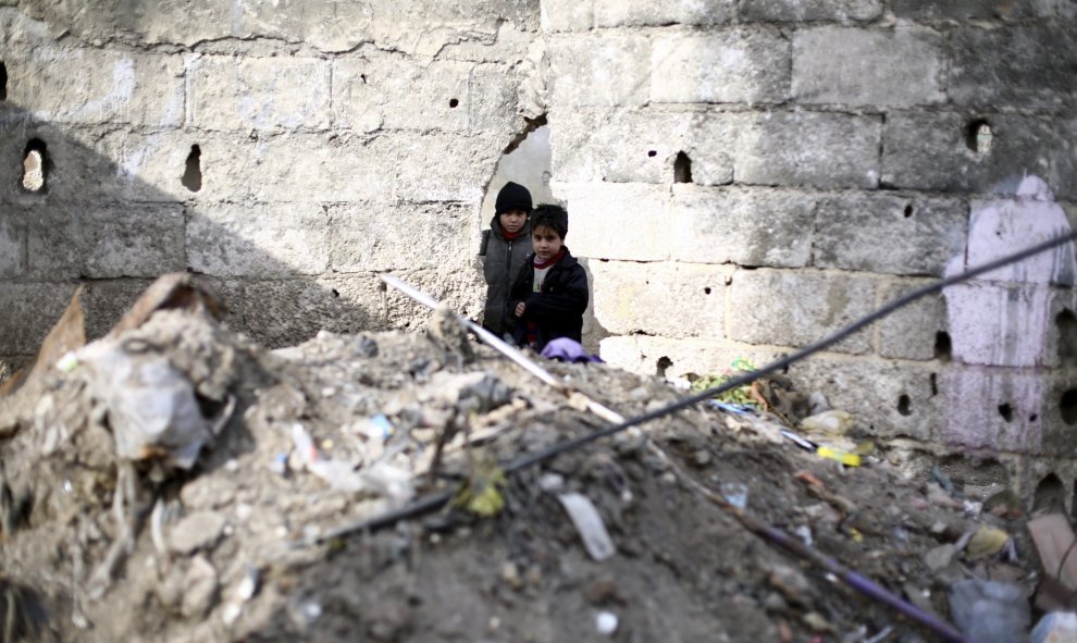 Dos niños miran a través de un agujero en un muro de una calle de Douma, afueras de Damasco, Siria, el 29 de diciembre del 2015. Más de cuatrocientas personas, entre heridos, rebeldes y civiles, fueron evacuadas ayer de varias ciudades asediadas sirias en