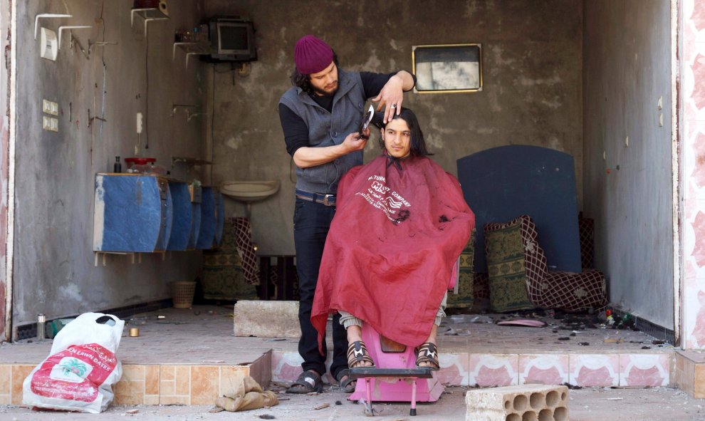 Un barbero le corta el pelo a un cliente fuera de su salón dañado por los rebeldes, en la ciudad de al-Ghariyah al-Gharbiyah town, Siria. REUTERS/Alaa Al-Faqir