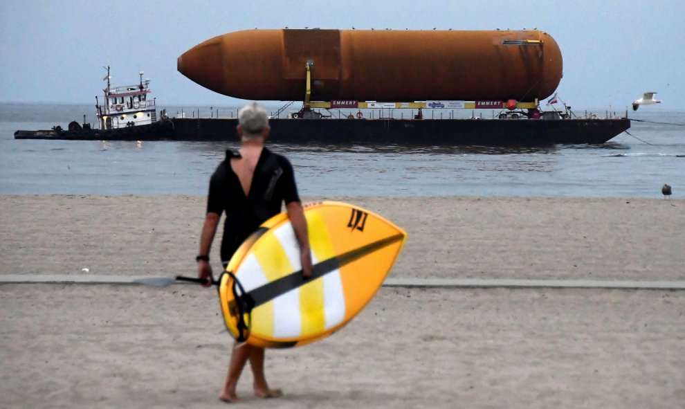 Un deportista de paddle board camina hacia el agua mientras que contempla un transbordador espacial que es transportado por medio de barcazas para su eventual colocación en el Centro de Ciencias de California en Marina del Rey, California. REUTERS/Gene Bl