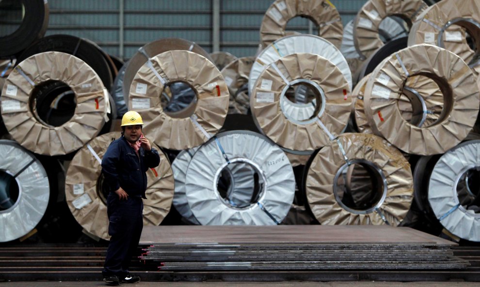 Un trabajador utiliza un teléfono móvil delante de bobinas y chapas de acero en un almacén de distribución en Urayasu. REUTERS/Toru Hanai