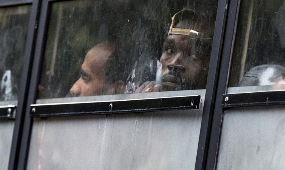 Varios migrantes sudaneses y eritreos miran por las ventanillas de un autobús mientras son desalojados por la policía durante el desmantelamiento de un campamento temporal de inmigrantes principalmente de Sudán y Eritrea, en la avenida Flandre en el norte