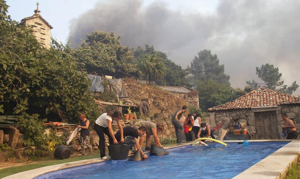 Un grupo de personas se baña en una piscina y mira a lo lejos como se acerca el incendio en Soutomaior (Pontevedra), muy cercano al núcleo urbano/EFE