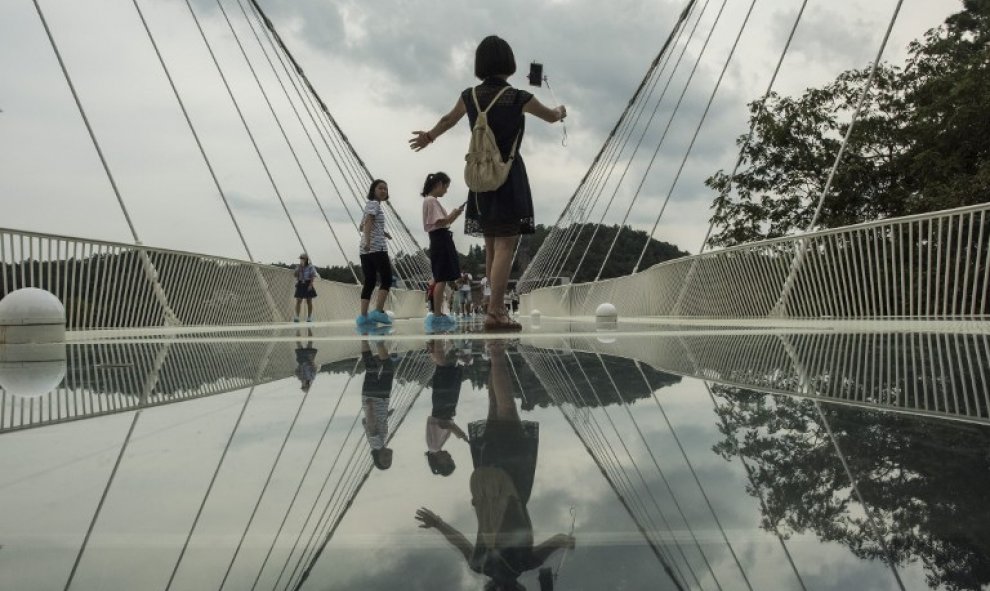 Una turista se hace un selfie sobre puente de cristal más largo y más alto del mundo sobre el valle del parque natural de Zhangjiajie, en la provincia china de Hunan. AFP/FRED DUFOUR