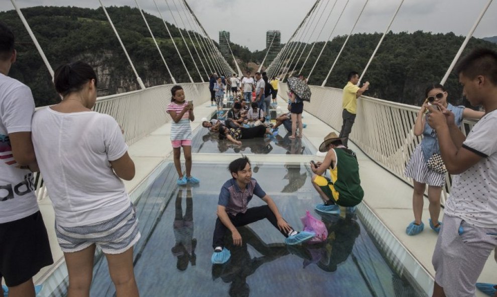 Un visitante posa para una foto sobre el suelo de cristal del puente más largo y más alto del mundo sobre el valle del parque natural de Zhangjiajie, en la provincia china de Hunan. AFP/FRED DUFOUR