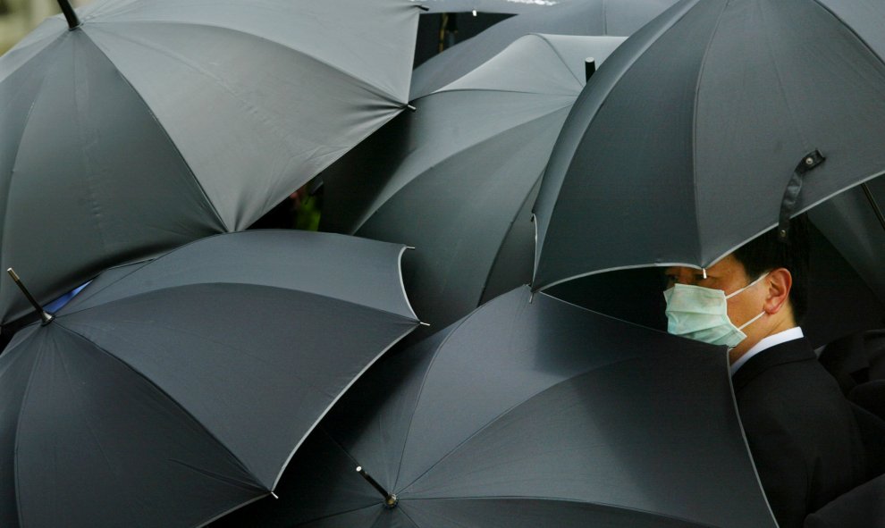 Un hombre lleva una máscara para protegerse del SARS (Síndrome Respiratorio Agudo Grave) se oculta bajo un paraguas durante el funeral del médico Tse-Yuen, en Hong Kong. REUTERS/Bobby Yip