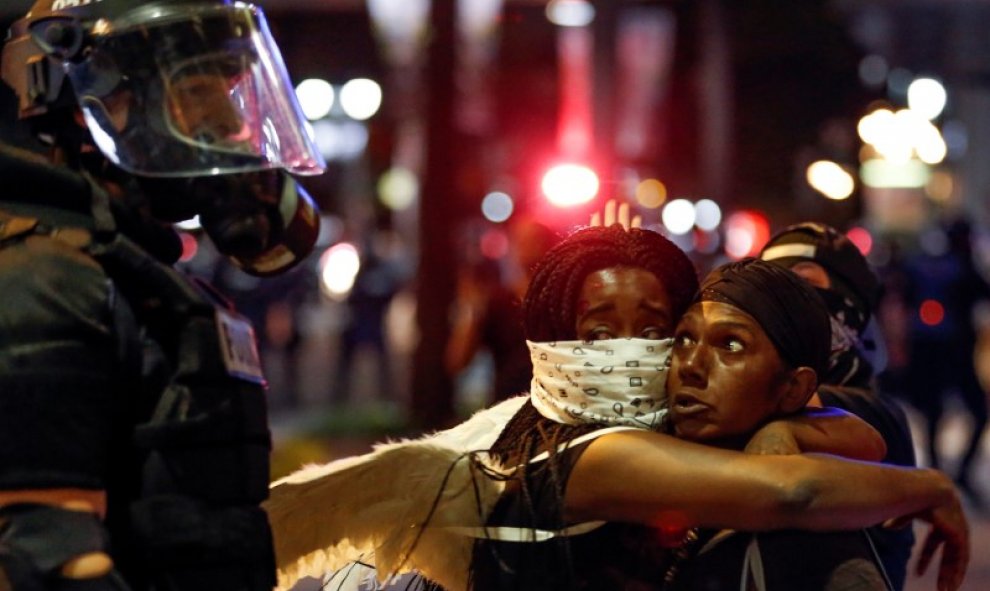 Dos mujeres que abrazan mientras miran a un oficial de policía en la zona alta de Charlotte, Carolina del Norte durante una protesta de los disparos de la policía contra Keith Scott, en Charlotte, Carolina del norte. REUTERS/Jason Miczek