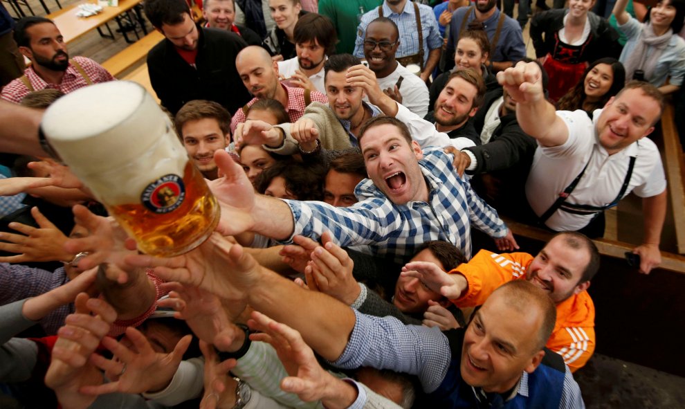 Visitantes de la 183 edición de la Oktoberfest en Munich intentan coger una de las primeras jarras de cerveza del festival/REUTERS