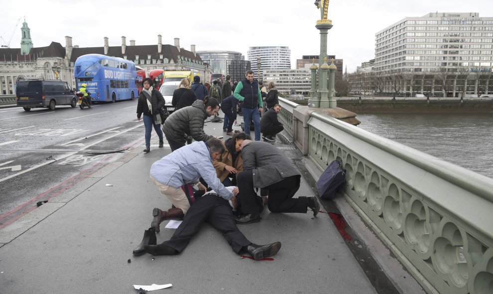 Varias personas atienden a uno de los heridos en el puente frente al Parlamento / REUTERS