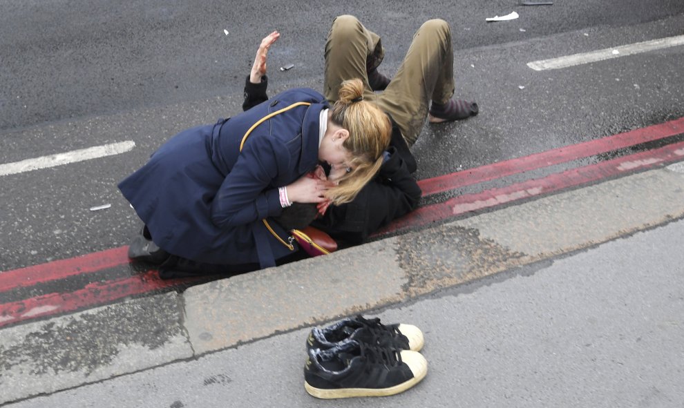 Una mujer atiende a otra en la acera / REUTERS