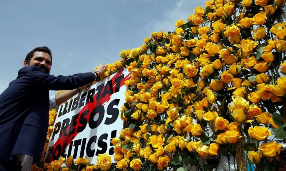 El presidente del Parlament, Roger Torrent, coloca una rosa amarilla en el panel que Omnium Cultural ha instalado en la plaza de Cataluña para pedir la libertad de los políticos independentistas presos. EFE