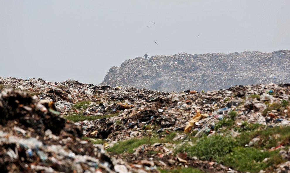 Un hombre recolecta materiales reciclables a medida que el humo se acumula en un vertedero en llamas con motivo del Día de la Tierra, en Calcuta. / Reuters