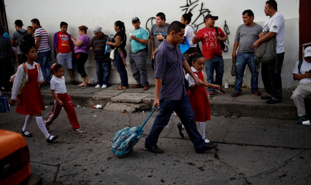 Niñas camino a la escuela pasan por delante de los migrantes que esperan ingresar a la Comisión Mexicana de Asistencia a Refugiados en Tapachula. / Reuters